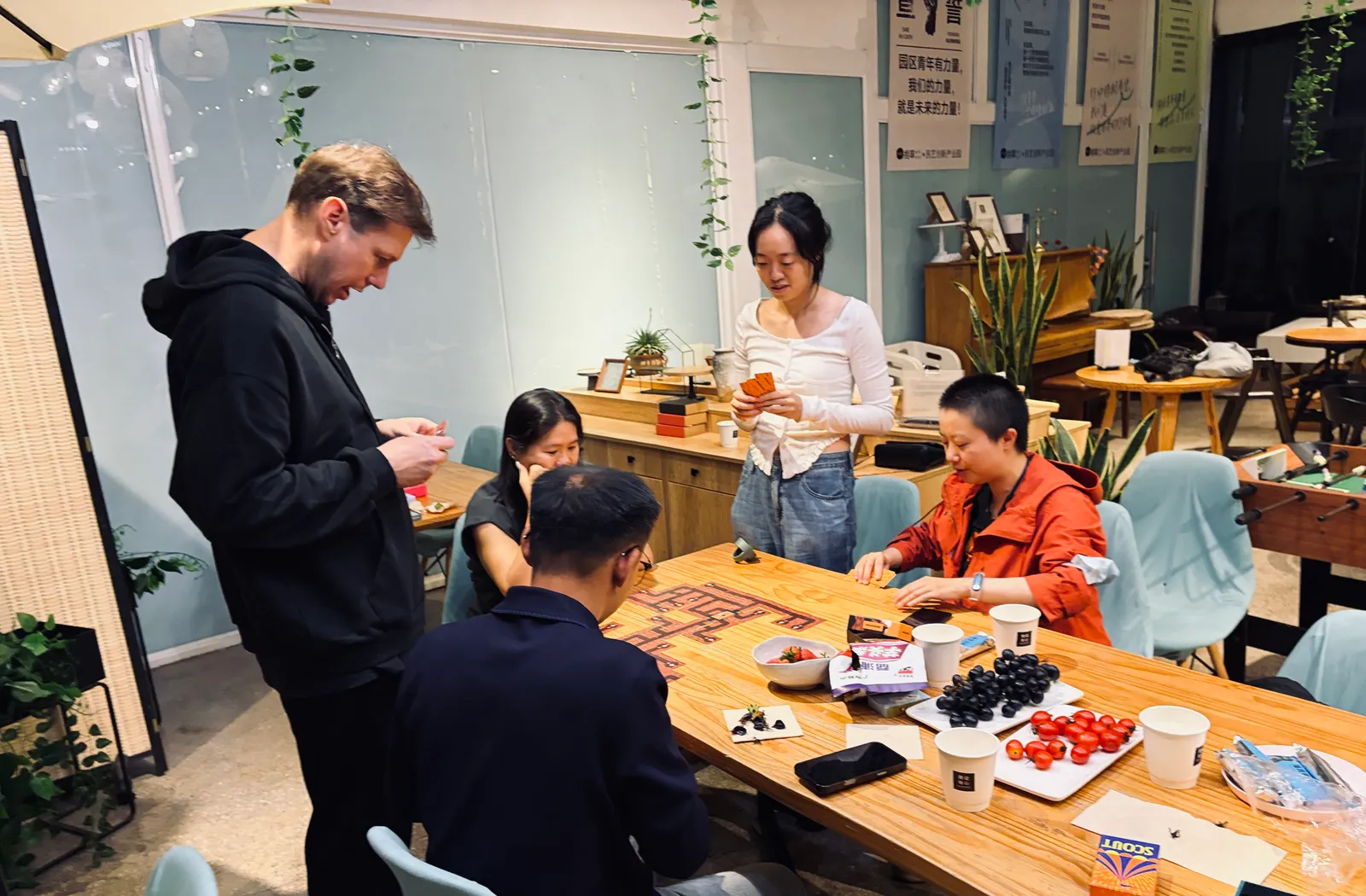Five players dealing cards at a table beside the cafe foosball table