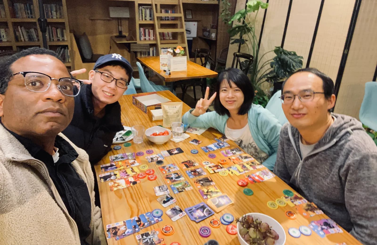 Four players mid-game, smiling for a selfie over a spread of cards and chips