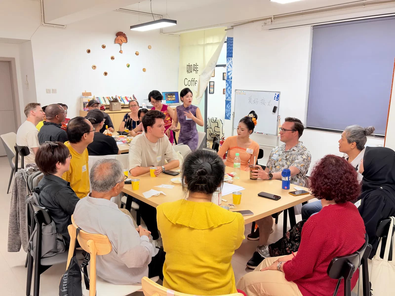A full table of locals and foreigners listening as a host in a qipao opens the session