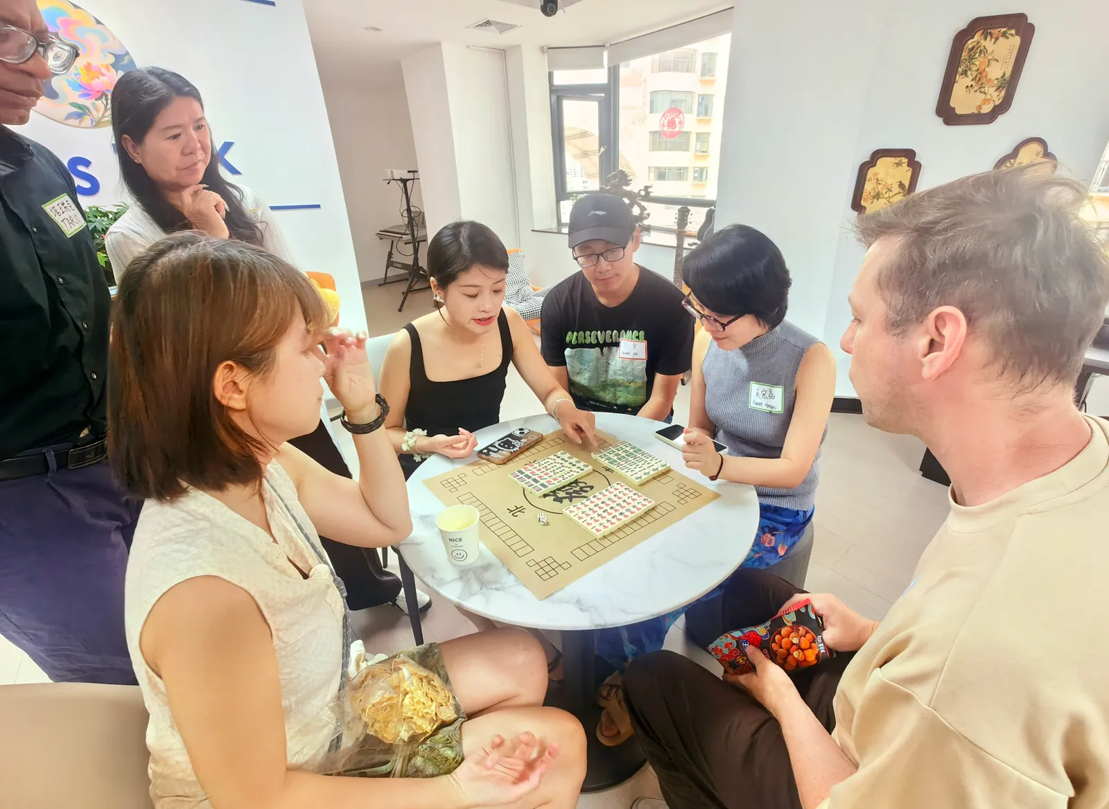 Learning mahjong around a small round table, tiles laid out on the mat
