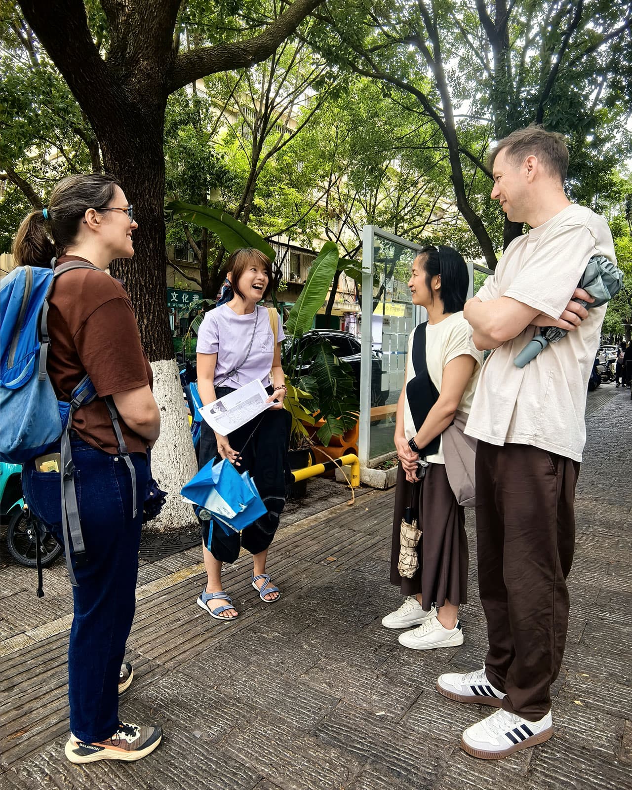 Kunming Walk group leader Dioni talking to a small group on a tree-lined path beside Green Lake, Kunming